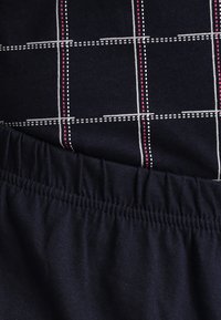 Marineblauwe stof met een geruit patroon in wit en roze. Voorzien van een elastische tailleband met een geplooide structuur aan de onderkant.