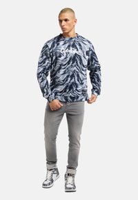 Navy and white patterned sweatshirt with a crew neck and logo, paired with gray jeans and high-top sneakers featuring a graphic design.
