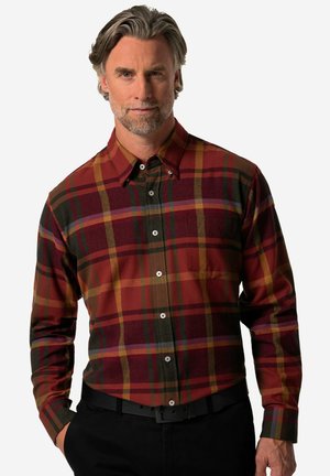 Camisa de cuadros rojo y verde, de botones y de manga larga, con tejido texturizado y un bolsillo en el pecho. Combinada con un cinturón negro.