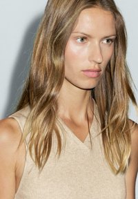 Top a spalla beige a costine con scollatura a V e dettagli in bottone, caratterizzato da un tessuto leggermente texturizzato e un design che scopre le spalle. Luce soffusa e naturale.