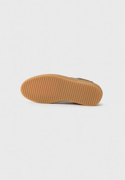 Sole of a sneaker, featuring a textured, ribbed design in light brown rubber. The upper section is visible in gray with multicolor accents.