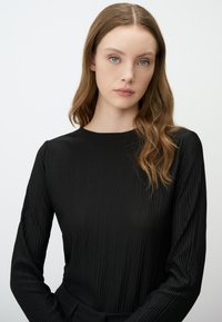 Schwarz langärmliges Oberteil mit geripptem Textur und rundem Halsausschnitt. Der Stoff wirkt glatt und figurbetont, ideal zum Layering.