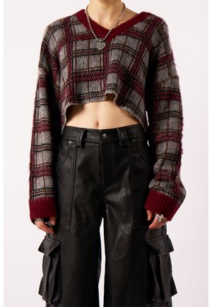 Personne portant un pull court à carreaux à manches longues et un pantalon cargo en cuir noir avec de grandes poches latérales.