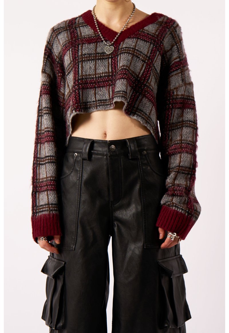Personne portant un pull court à carreaux à manches longues et un pantalon cargo en cuir noir avec de grandes poches latérales.