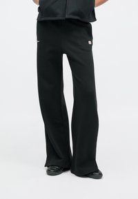 Czarne spodnie dresowe o luźnym kroju, wykonane z miękkiego materiału, z małym logo Nike oraz kontrastową naszywką z marką po boku.