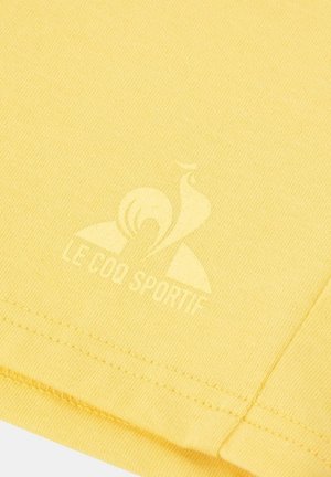 T-shirt en coton jaune avec un tissu texturé, des manches courtes et un logo subtil imprimé à l'avant dans une teinte plus claire.
