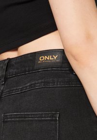 Crne traperice od denima s teksturiranim završetkom, s vidljivom oznakom marke ONLY na pojasu i detaljima na džepovima.