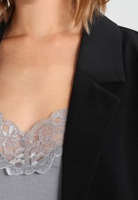 Svart kavaj med skarp skärning, lagd över en grå topp med en delikat, scallop-lace halsringning. Slät tyngd.