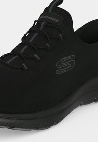 Μαύρο αθλητικό παπούτσι Skechers με ελαστικά κορδόνια χωρίς δέσιμο, άνω μέρος από δίχτυ και υφή στη σόλα.