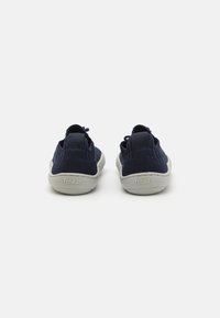Chaussures en mesh bleu marine avec une tige texturée, semelles en caoutchouc gris plat et une languette à l'arrière. Logo de la marque "froddo" sur le talon.