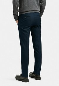 Marinblå byxor med skräddarsydd passform, tillverkade av slät tyg. Har två bakfickor och en borstad grå tröja ovanpå.