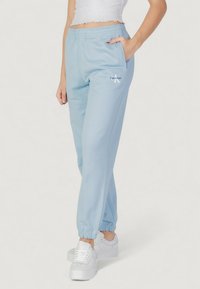 Světle modré tepláky s elastickým pasem a manžetami na kotnících. Mají boční kapsy a malé bílé logo "Calvin Klein". Šitý z bavlněné směsi.