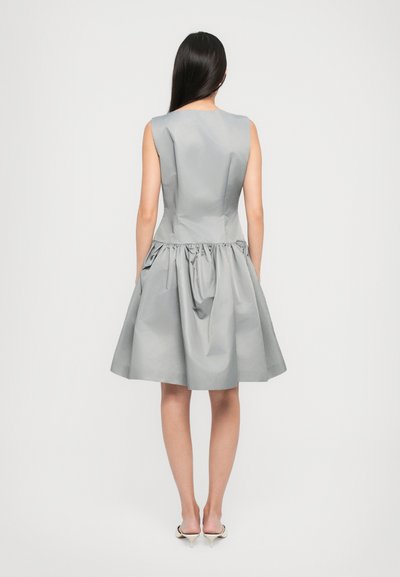 Szürke, ujj nélküli ruha, amely testre szabott felsőrésszel és redőzött szoknyával rendelkezik. Simáló anyagból készült, az alakja enyhén bővülő. Minimalista dizájn.