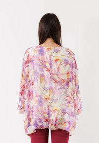 Blusa leggera e floreale in tessuto trasparente di colori pastello, con maniche morbide e orlo curvo, abbinata a pantaloni burgundy aderenti.