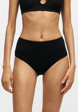 Kvinde iført sort høj talje ribbet undertøj og matchende sort crop top med rund udskæring nær halsudskæringen.