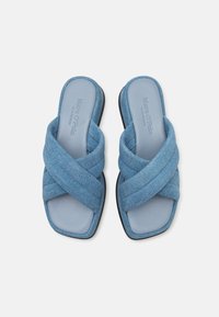 Infradito incrociati in denim blu con una soletta liscia di un azzurro chiaro e una suola nera piatta. Il tessuto texturizzato aggiunge dettaglio al design.
