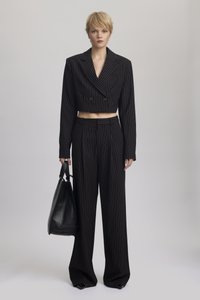 Blazer nero a righe con doppio bottone e pantaloni a righe a gamba larga. Il modello tiene una borsa a tracolla in pelle nera.