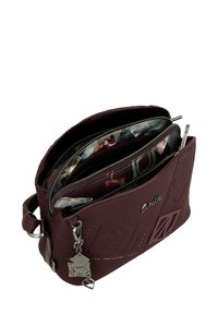 Bolso de mano burdeos hecho de material texturizado, con múltiples compartimentos con cremallera y un charm decorativo de metal. Acentuado con un forro estampado.