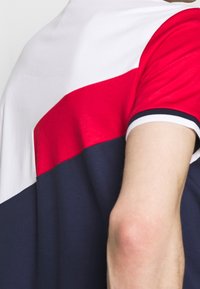 Pánská polo košile s horizontálními pruhy v červené, bílé a námořnické modré. Vyrobena z měkké tkaniny s kontrastním límečkem a krátkými rukávy.