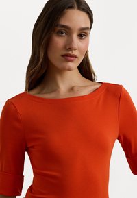 Rode fitted top met een bootnek en korte omgeslagen mouwen. Glad textuur en naadloos ontwerp in een levendige, effen kleur.