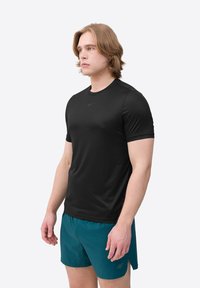 Zwart sportshirt met korte mouwen en ronde hals, gemaakt van ademend materiaal, gecombineerd met teal korte broek. Bevat subtiele logodetails.