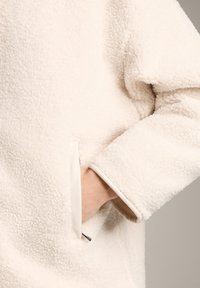 Pullover in pile crema con tessuto testurizzato, vestibilità rilassata, tasca laterale e rifiniture a contrasto sui polsini. Aspetto morbido e caldo.