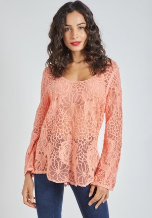 Blusa de encaje melocotón con estampado floral, de mangas largas, escote en forma de barco y dobladillo ligeramente acampanado. Textura transparente; corte relajado.