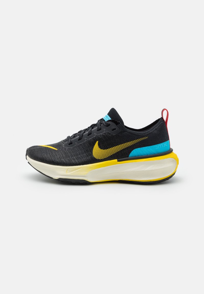 Chaussure de running Nike noire et jaune avec semelle blanche épaisse, accent bleu près du talon, languette rouge et logo swoosh jaune sur le côté.