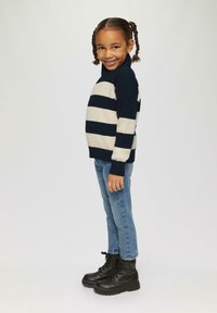 Sweter w paski typu golf w kolorach granatowym i kremowym, wykonany z teksturowanej tkaniny. Połączony z niebieskimi dżinsami i czarnymi botkami za kostkę. Wyrazisty stój casualowy.