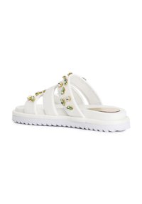 White multi-strap sandals with textured soles, embellished with green and clear gemstones. Lightweight design suitable for casual wear.