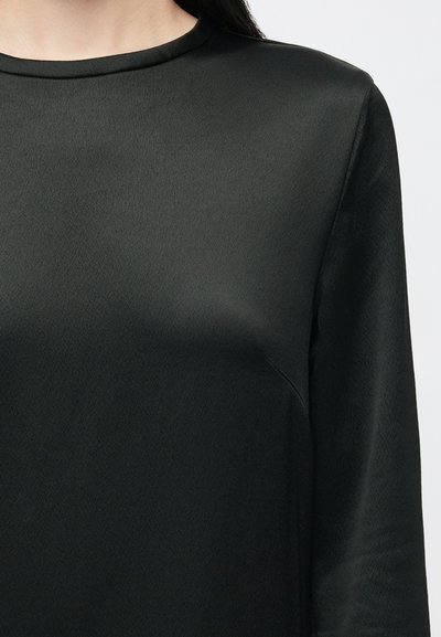 Blusa preta de mangas longas feita de tecido liso com decote redondo e uma textura subtil, apresentando uma silhueta ajustada.