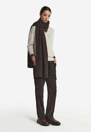 Un pull gris clair avec un décolleté en V, une écharpe marron foncé, un pantalon cargo marron foncé et des chaussures à lacets marron. Textures douces et look en couches.