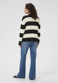 Un pull rayé noir et blanc avec une coupe décontractée, des manches longues et des poignets côtelés, associé à un jean en denim bleu évasé.