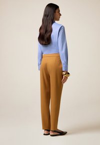 Chemise bleu clair à manches longues, pantalon slim-fit moutarde et ballerines noires. Bracelet en or au poignet, tissu texturé et design ajusté.