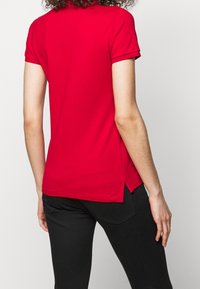 Polo shirt rouge à manches courtes avec ourlet droit et fentes latérales. Fabriqué en tissu lisse, avec un col classique et une coupe ajustée.