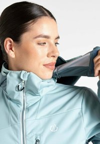 Hellblaue Softshell-Jacke mit hohem Kragen, Front-Reißverschluss und verstellbaren Manschetten. Hat ein Logo auf der Brust und eine glatte Textur.