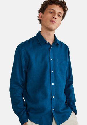 Chemise boutonnée bleu canard en lin, dotée d'un col pointu, de manches longues et d'une poche poitrine. Des boutons blancs apportent un contraste.