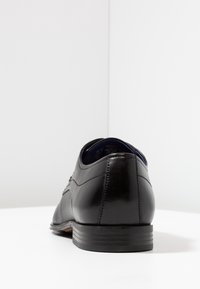 Chaussure habillée en cuir noir avec une finition lisse, bout rond et coutures détaillées. Présente un talon bas et texturé avec un intérieur bleu.