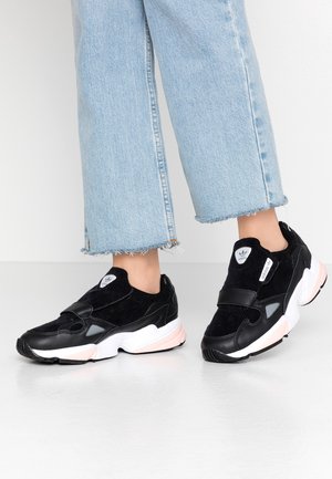 Stopy w czarno-białych sneakersach Adidas typu slip-on zestawione z jasnoniebieskimi, krótkimi dżinsami z postrzępionymi krawędziami.