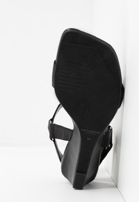 Sandale à talon haut noire avec un bout carré, une bride autour de la cheville et une semelle texturée marquée "Vagabond Shoemakers 37".