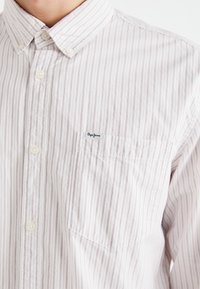 Button-up shirt in white with red vertical stripes. Features a pocket and a small logo on the chest. Made from lightweight fabric.