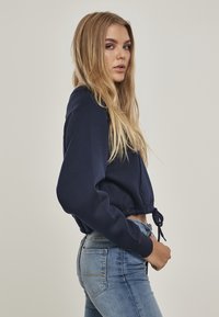 Felpa cropped blu navy con maniche lunghe, orlo con cordoncino e texture morbida, abbinata a jeans aderenti in denim azzurro.