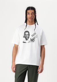 White cotton T-shirt featuring a black graphic print of a man with a guitar and text "the new originals." Short sleeves and relaxed fit.