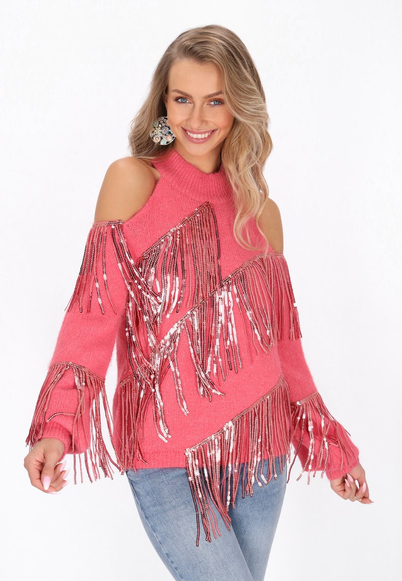 Różowy sweter dziany z ażurowym wzorem na ramionach, z długimi frędzlami i metalicznymi akcentami. Miękka tekstura i luźny krój zwiększają komfort noszenia.