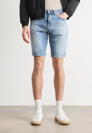 Lichtblauwe denim shorts met een rechte snit, gescheurde zoom en subtiele vervaging. G gedragen met witte sneakers en witte enkelkousen.