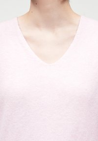 Απαλή και ροζ πουλόβερ με σχέδιο V-λαιμού. Το ύφασμα φαίνεται ελαφρύ και λεπτό, κατάλληλο για casual ντύσιμο.