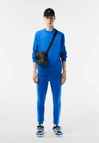 Blå sweatshirt och byxor i mjukt material, tillsammans med en svart axelväska och blåa och vita sneakers, med en elegant design.