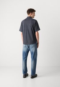 Πουκάμισο κοντομάνικο καρό σε σκούρο μπλε και άσπρο, συνδυασμένο με ανοιχτό μπλε τζιν. Φτιαγμένο από βαμβακερό υλικό με άνετη εφαρμογή και κλασικό γιακά.