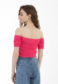 Lyserød strikket top med off-shoulder-design, teksturmønster og korte ærmer, parret med højtaljede blå denimjeans.
