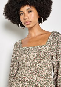 Grün geblümte Bluse mit quadratischem Ausschnitt, langen Ärmeln und einem gerafften Oberteil mit kleinen weißen und rosa Blumen.